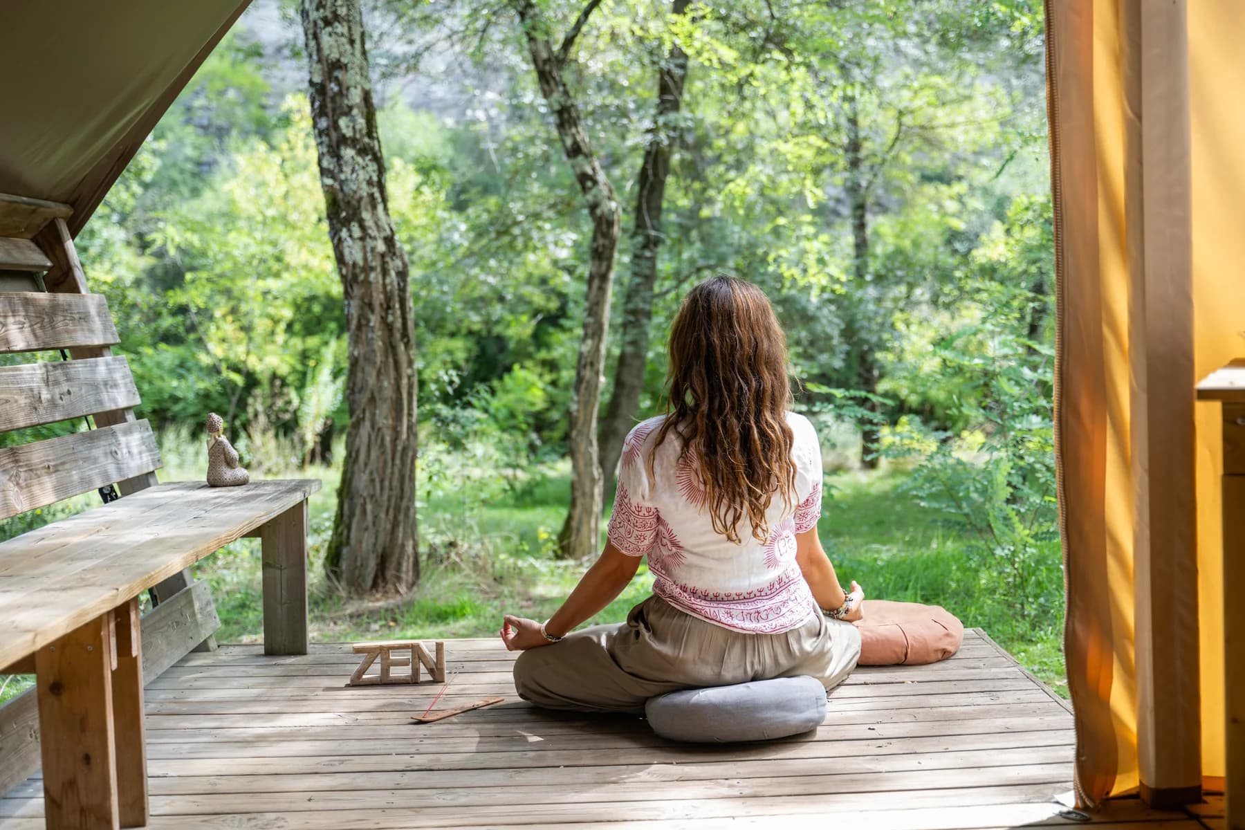 Femme en méditation, assise en lotus sur la terrasse d'une tente lodge face à la forêt
